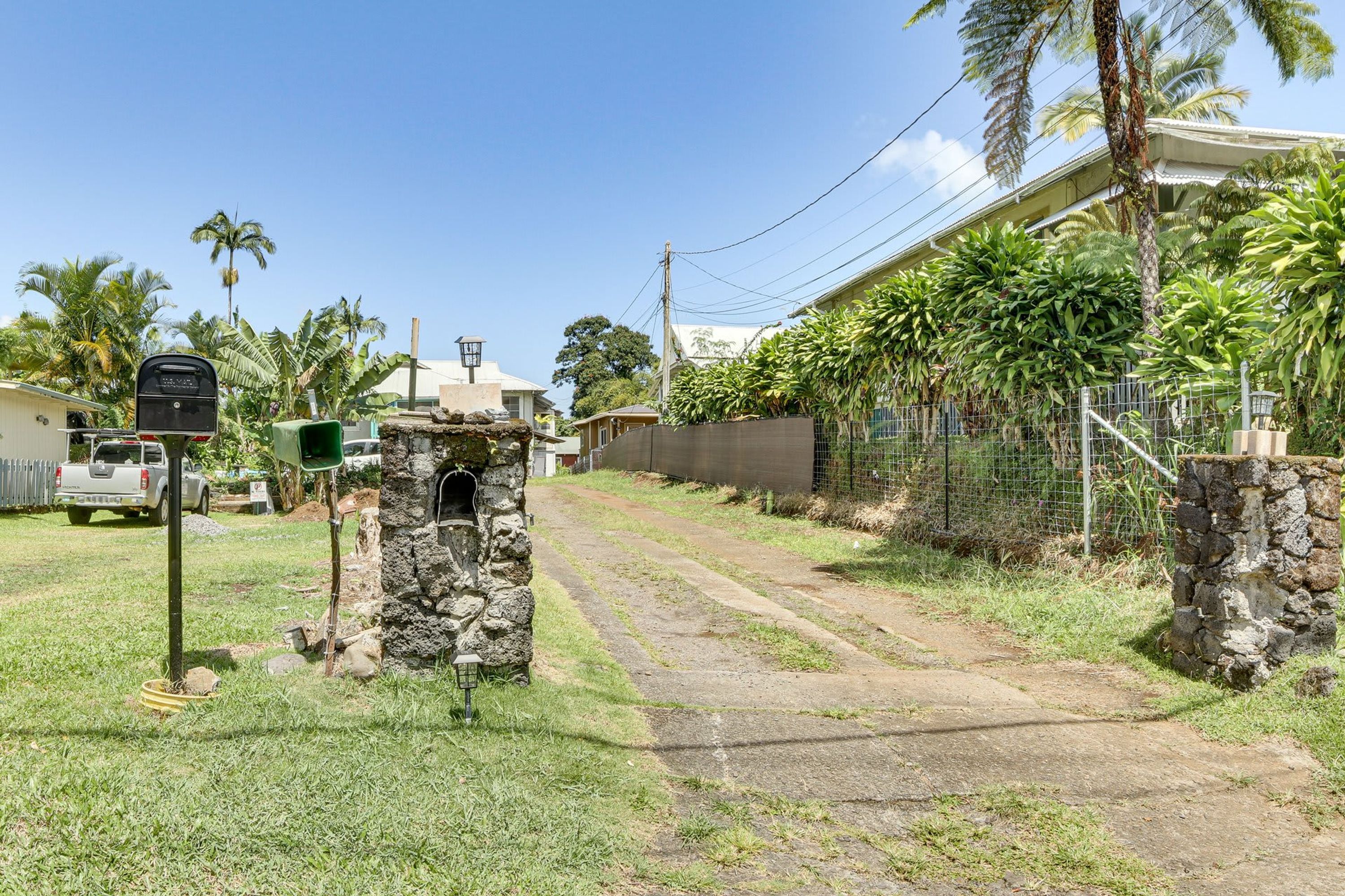 Zona residencial con un buzón de piedra, un camino de entrada pavimentado y una casa con patio cercado.
