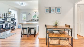 A modern kitchen with a central island, wooden flooring, and a dining area with a table and chairs.