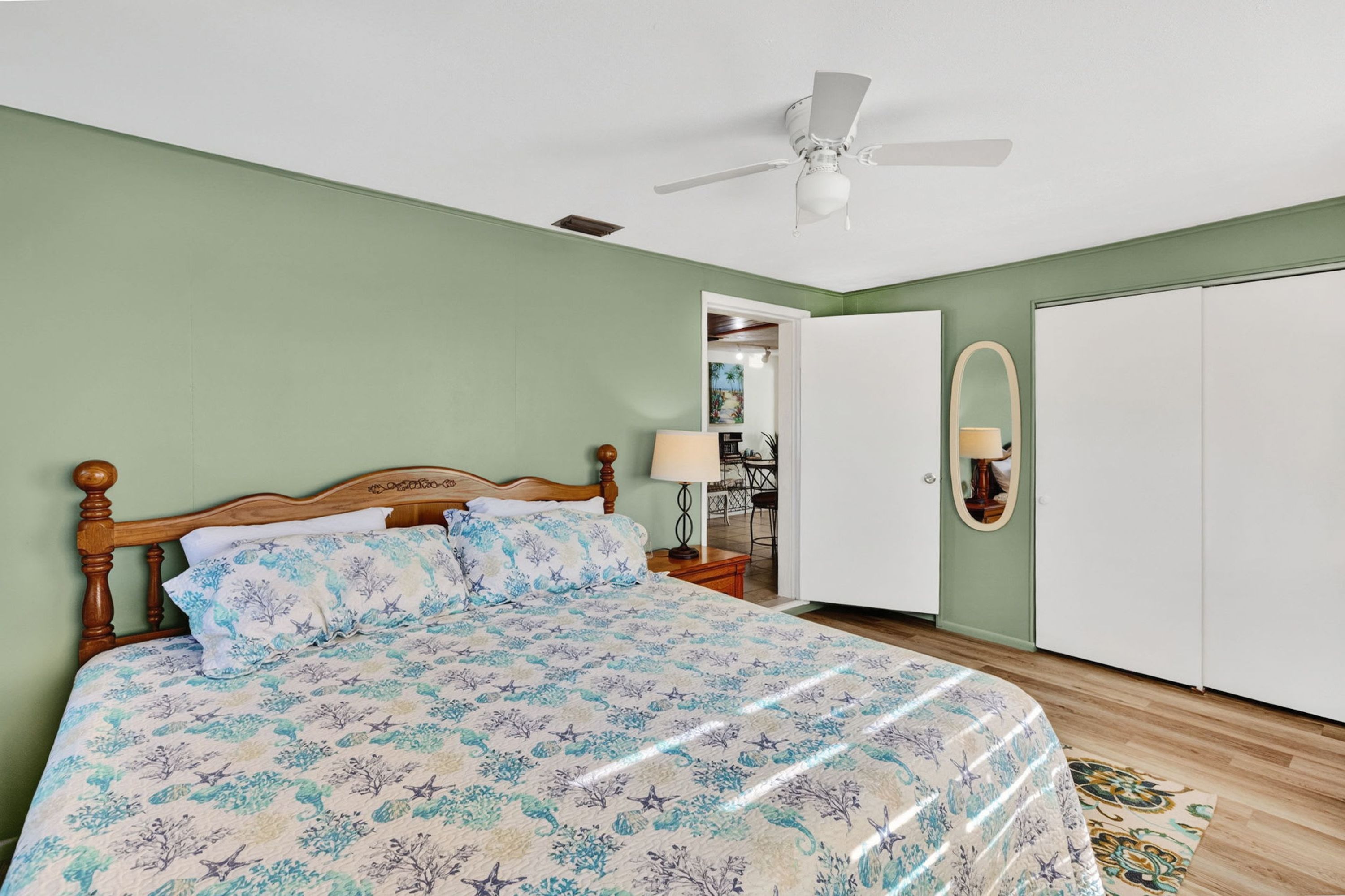 A bedroom with a bed, a ceiling fan, a wardrobe, and a door leading to another room.
