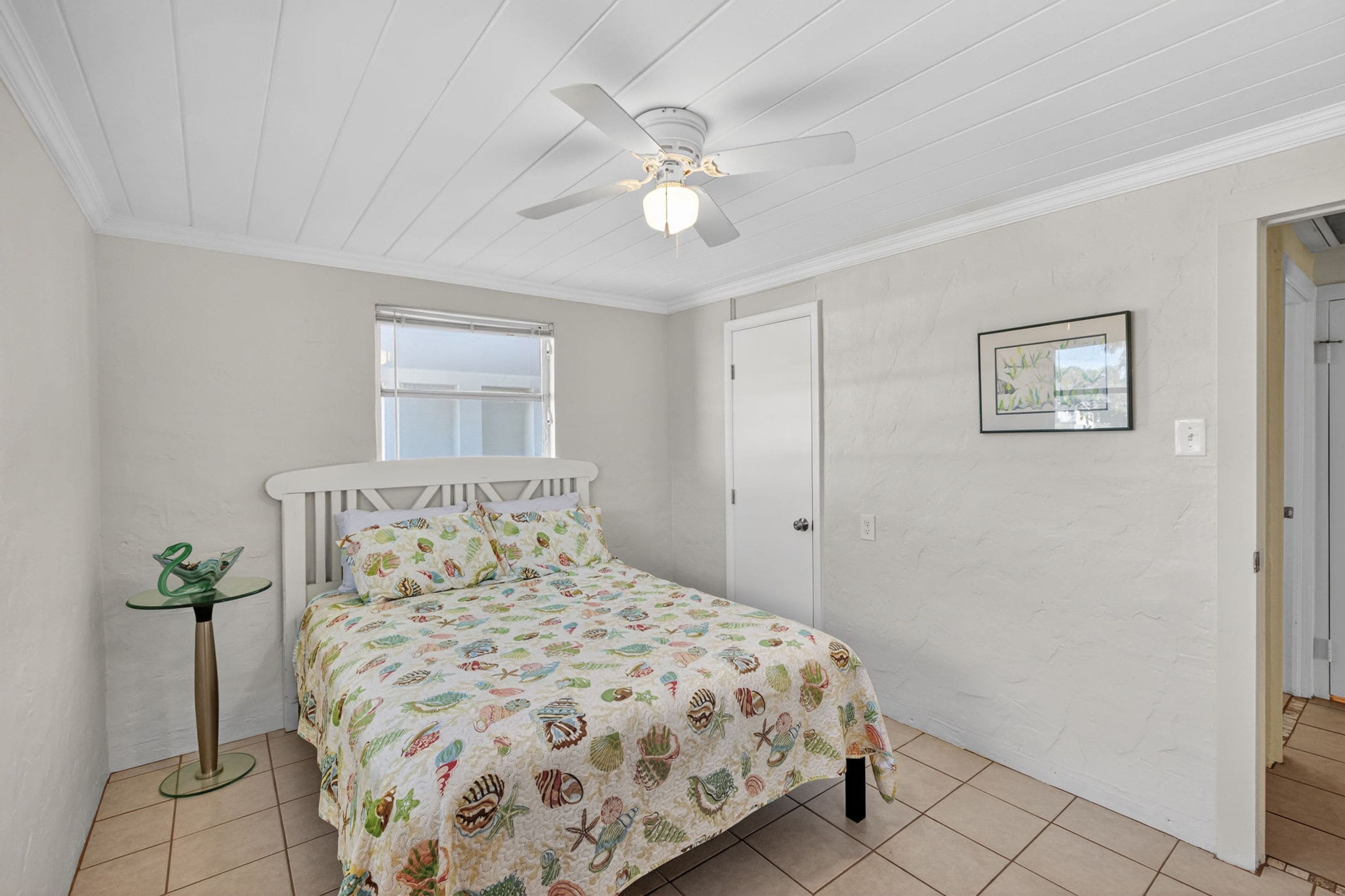 A bedroom with a bed, a ceiling fan, a window, and a door.
