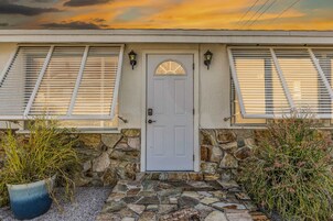 Una casa con fachada de piedra, una puerta blanca y contraventanas en las ventanas.