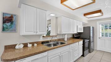 A kitchen with white cabinets, a stainless steel sink, a dishwasher, and a refrigerator.