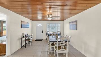 A dining area with a wooden ceiling, white walls, and a large window with blinds.
