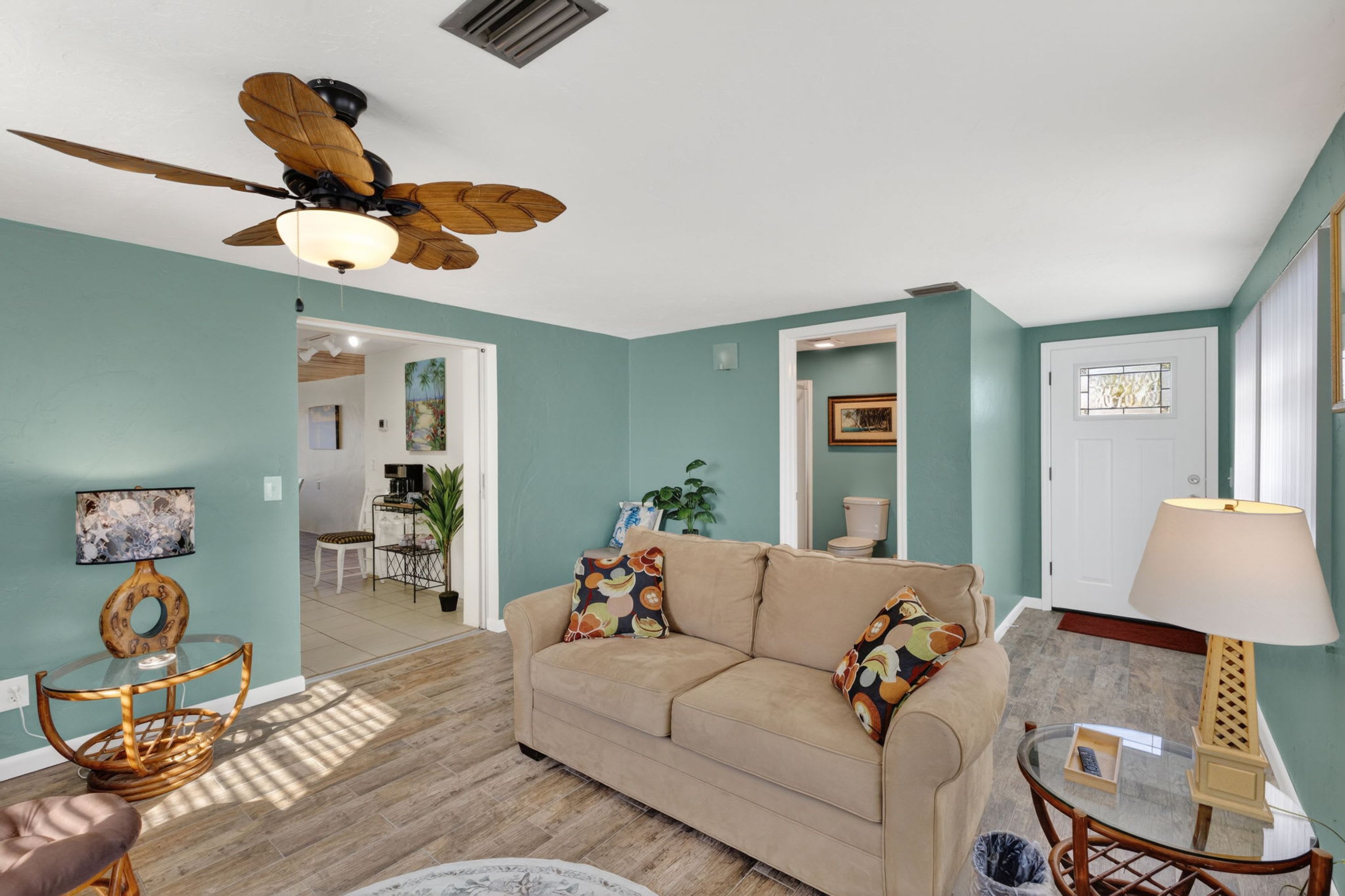 A living room with a ceiling fan, a beige sofa, a glass coffee table, and a wooden side table.