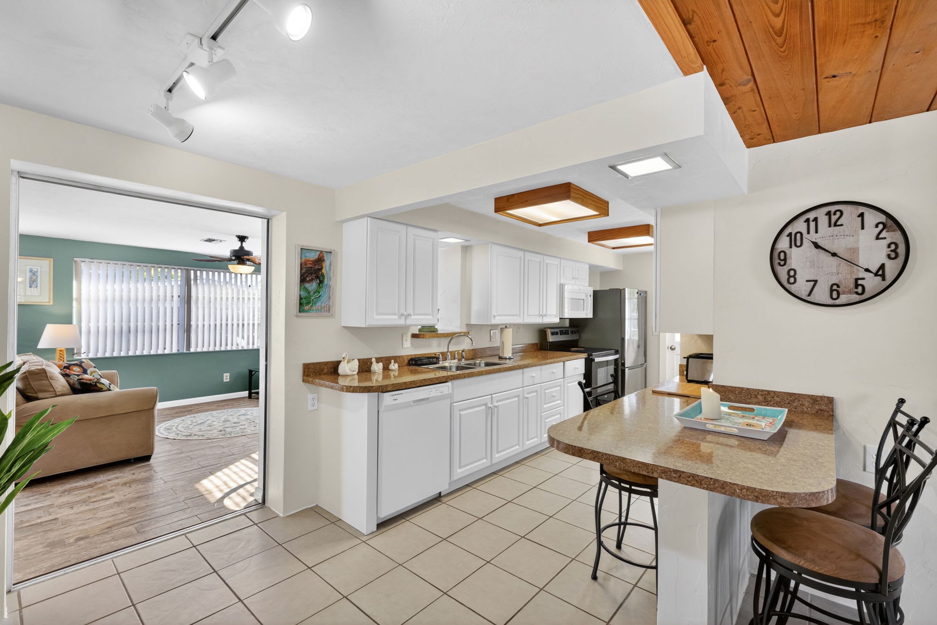 A modern kitchen with white cabinets, a wooden ceiling, and a built-in island with bar stools.