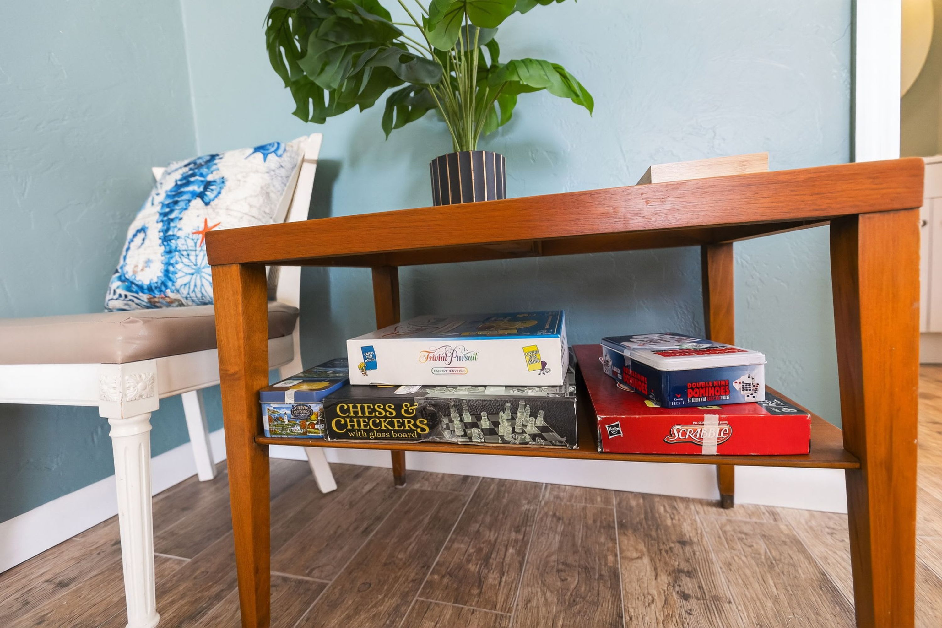 Une table en bois sur laquelle on trouve un jeu d’échecs avec un plateau en verre, ainsi que des jeux de société comme le Scrabble et d’autres jeux de plateau.
