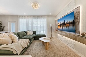 A modern living room with a sectional sofa, a round coffee table, and a large flat-screen TV mounted on a textured wall. - Family Townhouse With Private Pool and Themed Kids Rooms Windsor Cay (Clermont)