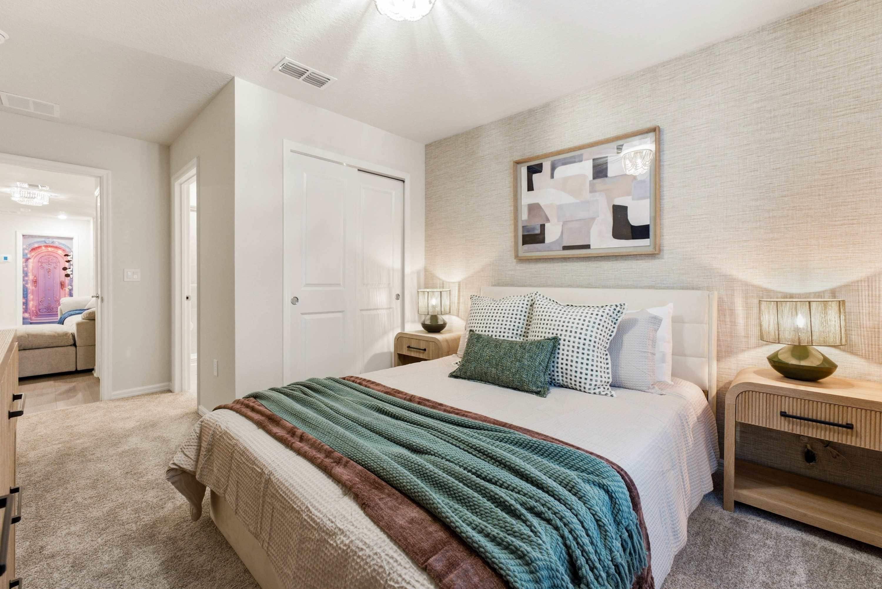 A bedroom with a bed, two bedside tables, a wall-mounted artwork, and a door leading to another room.