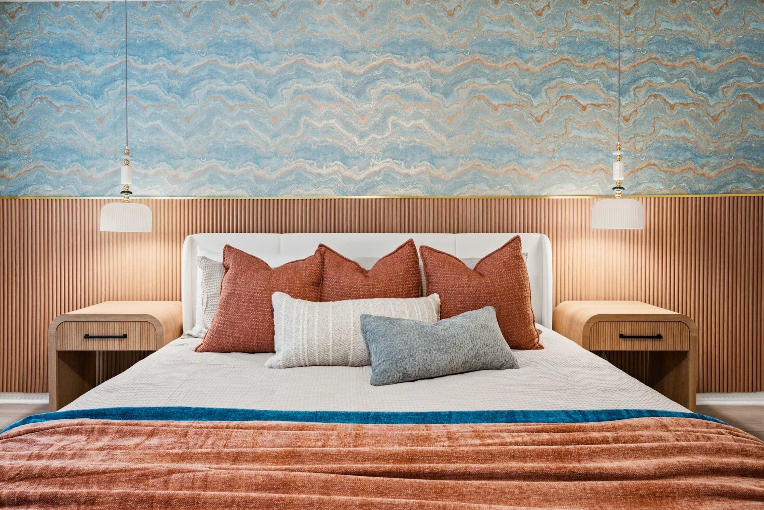 Ein ordentlich bezogenes Bett mit einem weißen Kopfteil, mehreren Kissen und einer gestreiften Decke.