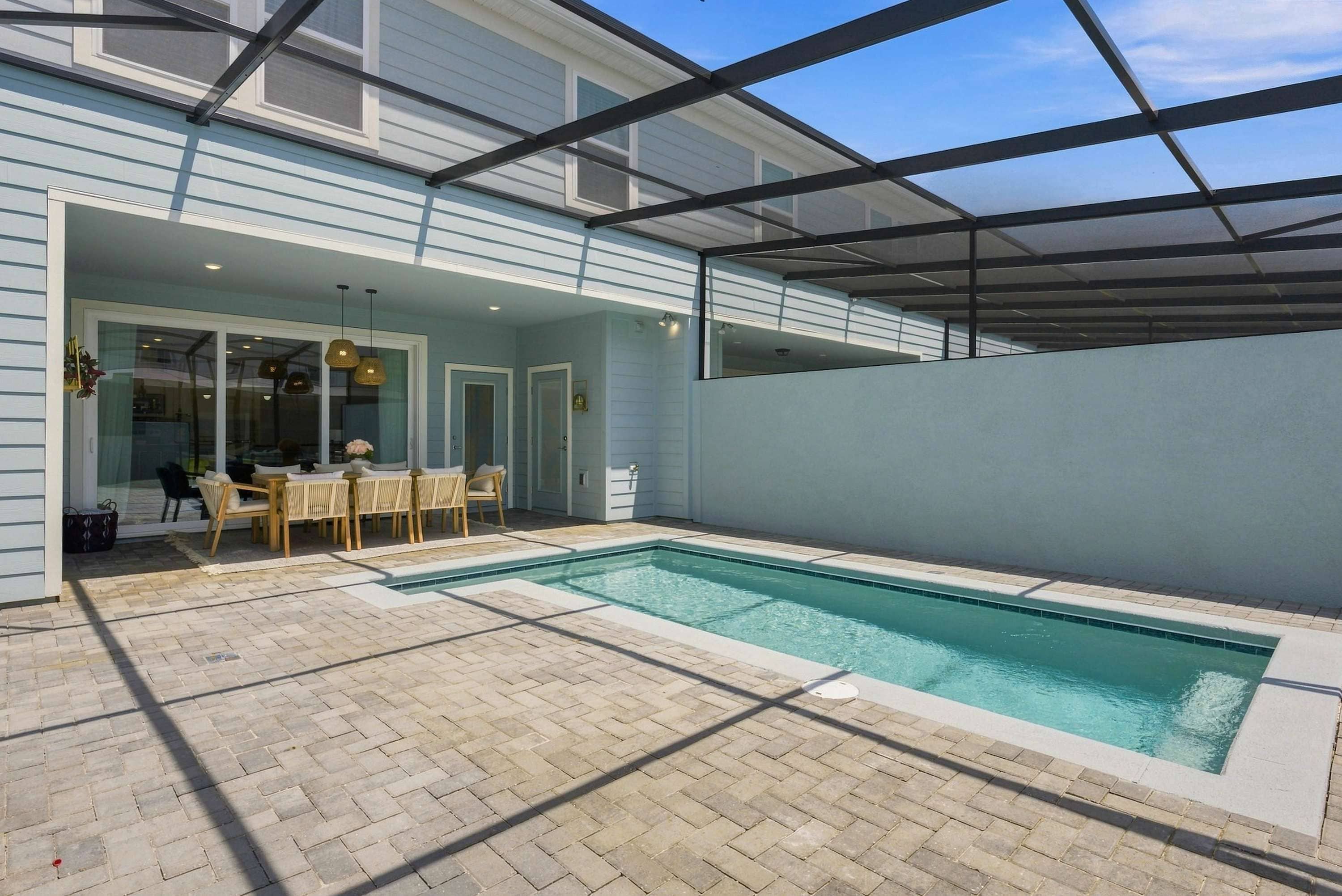 Una piscina con zona de patio, área de estar cubierta y vista a una casa.
