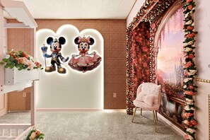 Une pièce avec une grande fresque murale, une chaise blanche et un mur décoratif orné de motifs représentant Mickey et Minnie Mouse.