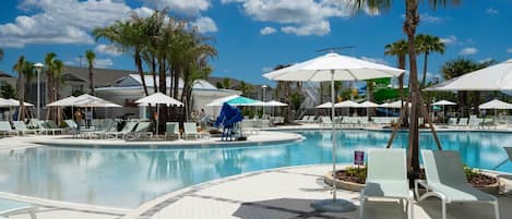A pool area with lounge chairs and umbrellas, surrounded by palm trees and a clear sky.