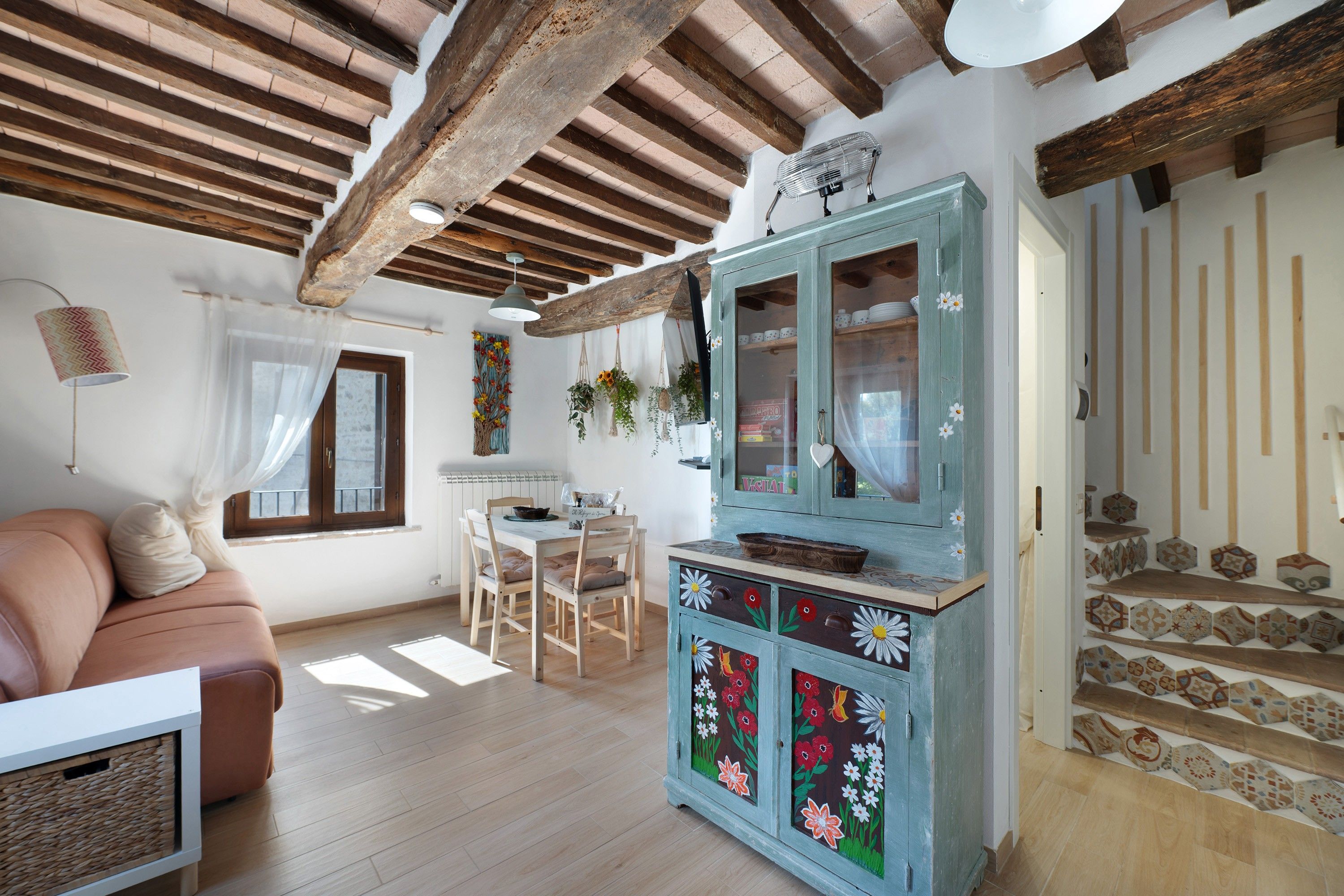 Una sala de estar acogedora con techo de madera, un comedor con mesa y sillas, y un aparador decorado con motivos florales.