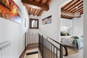 A staircase with a wooden handrail leading to a bedroom with a bed and a window.
