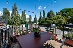 An outdoor seating area with a table and chairs, surrounded by potted plants and a view of the street.