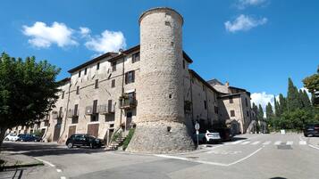Un edificio storico in pietra con una torre imponente, una strada antistante e auto parcheggiate.