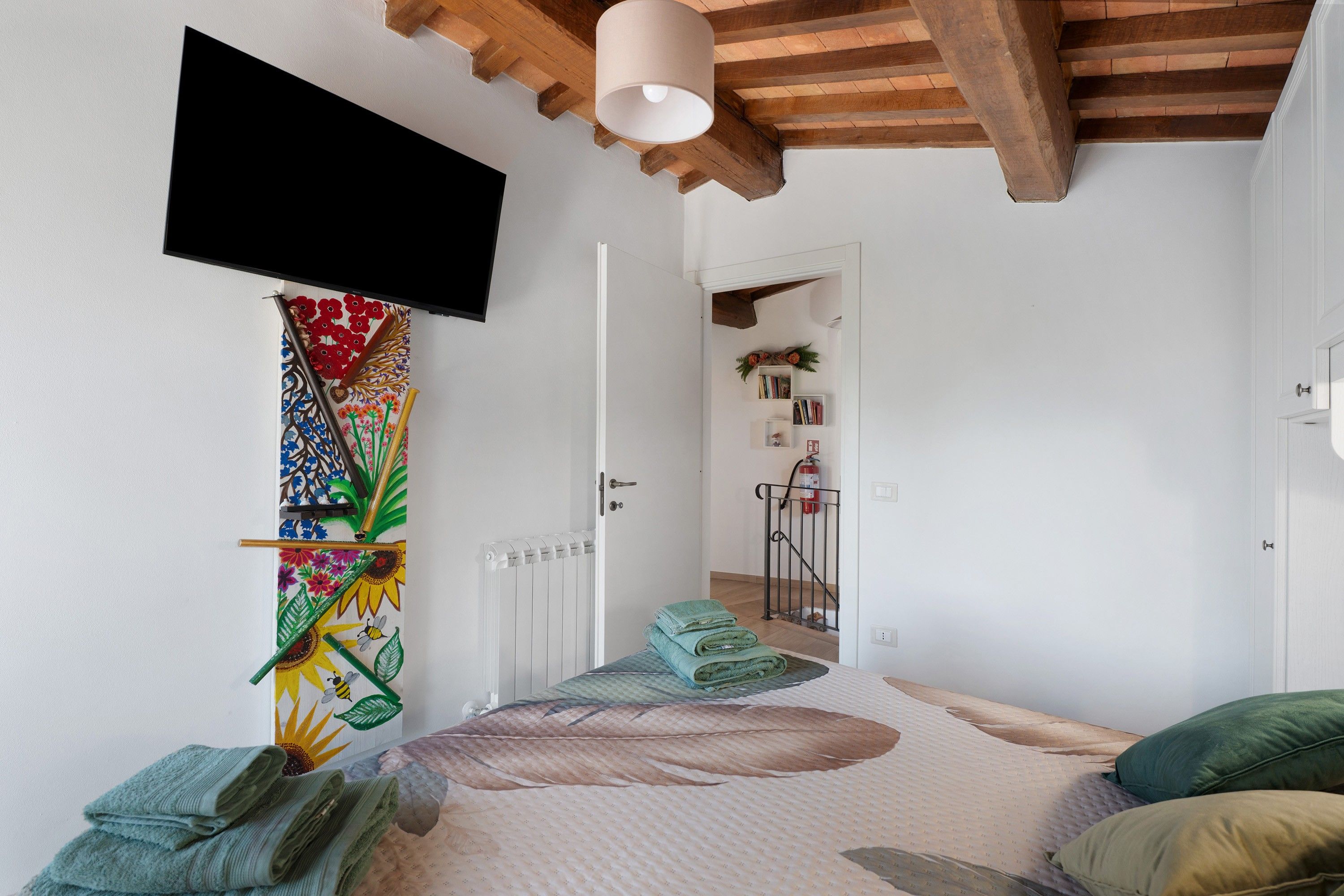 Ein Schlafzimmer mit einem Bett, einem an der Wand befestigten Fernseher, einer Heizung und einer Tür zu einem anderen Raum.
