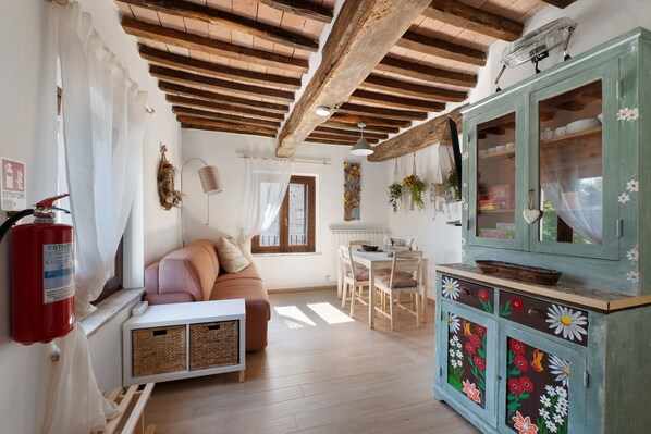 A cozy living room with a wooden ceiling, a sofa, a dining table, and a cabinet with floral designs.