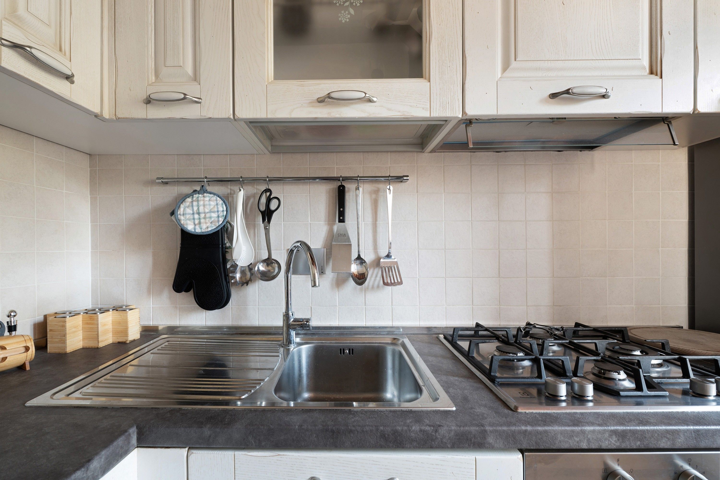 Una cocina con un lavamanos de acero inoxidable, una estufa a gas y diversos utensilios colgados en la pared.