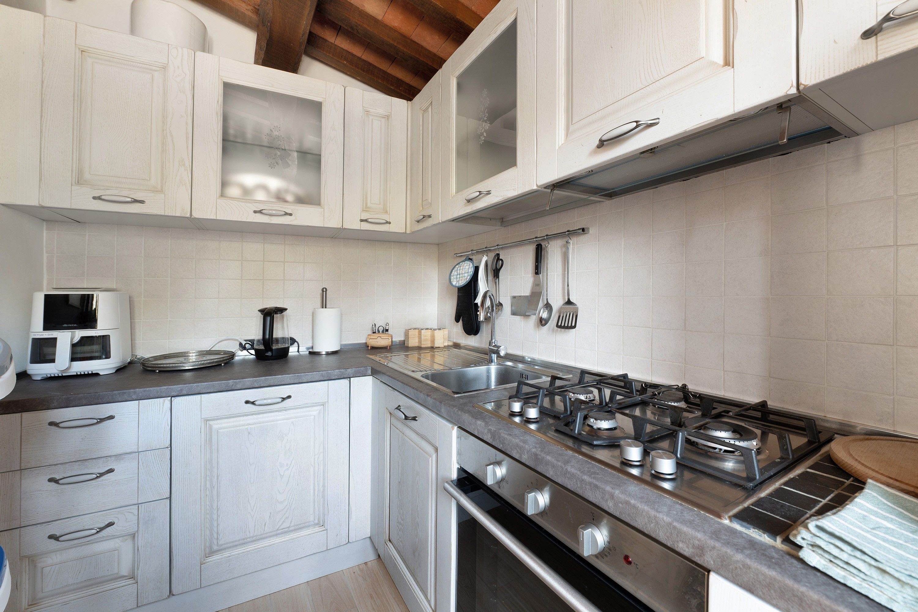 Una cucina con mobili bianchi, un piano cottura in acciaio inossidabile e una parete rivestita in piastrelle.