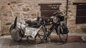 Una bicicleta estacionada junto a un muro de ladrillo, con un bolso etiquetado 'Consul' y un objeto metálico en el suelo.