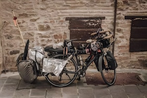 A bicycle parked against a brick wall with a bag labeled 'Consul' and a metal object on the ground.