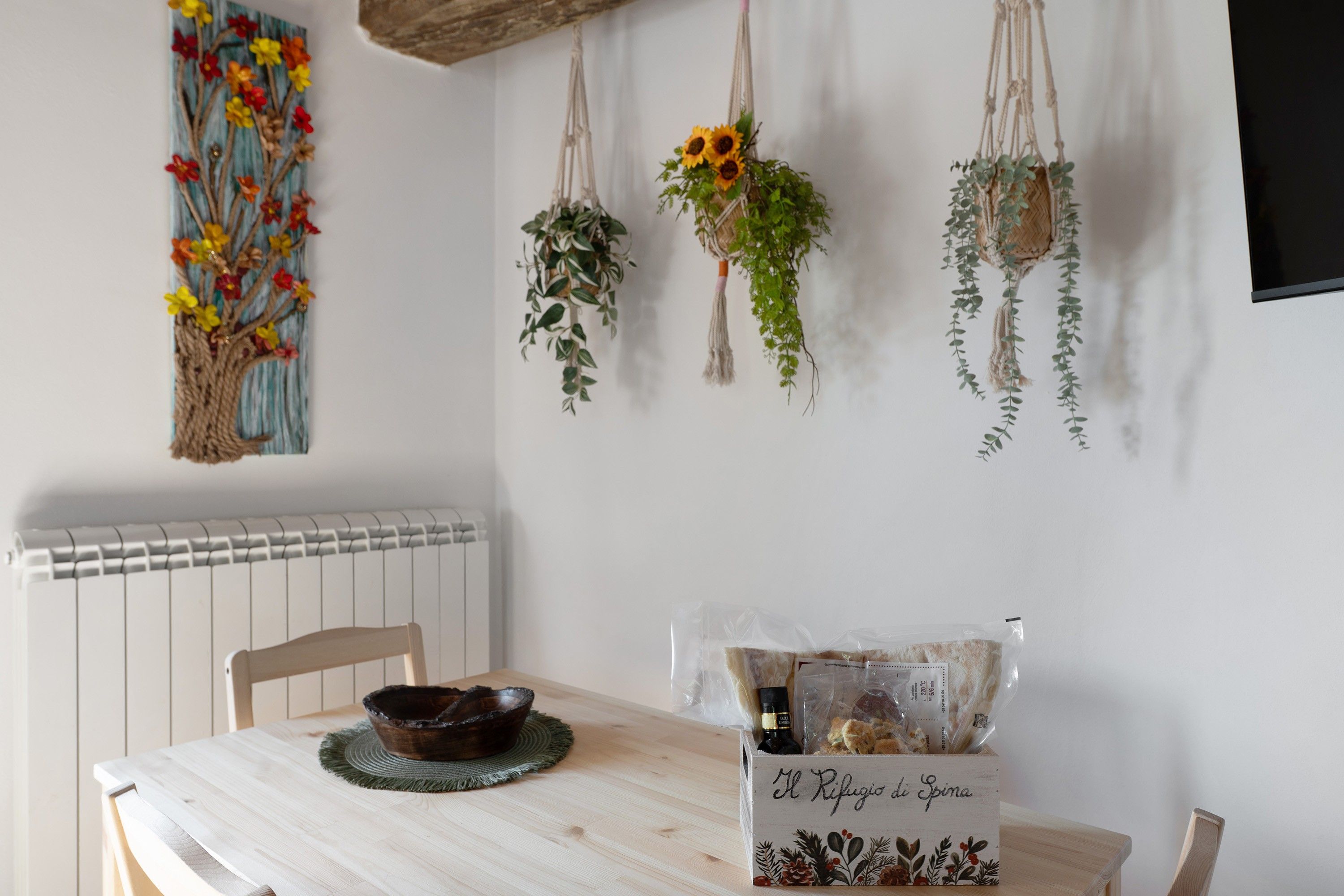 Un comedor con una mesa de madera, un cuenco y una planta decorativa colgante de macramé.