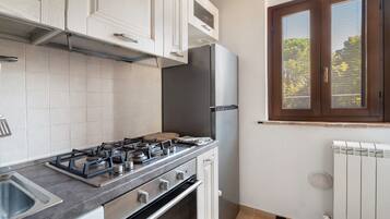 Una cocina con armarios blancos, cocina a gas, refrigerador y ventana con persianas.