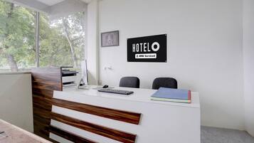Mostrador de recepción de hotel con un cartel que indica servicio OYO. Hay dos sillas, un teclado, un ratón y un libro en el mostrador.