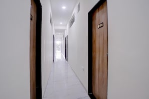 A corridor with wooden doors, white walls, and a tiled floor.