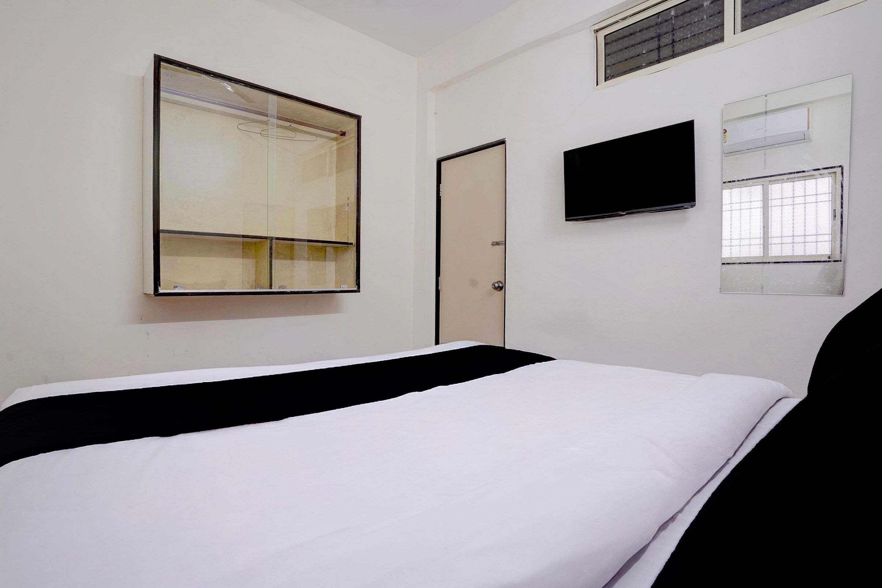 A room with a bed, a television, a window with blinds, and a door.