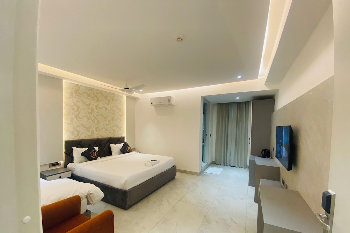 A modern hotel room with a bed, a seating area, a television, and a bathroom visible through a door.
