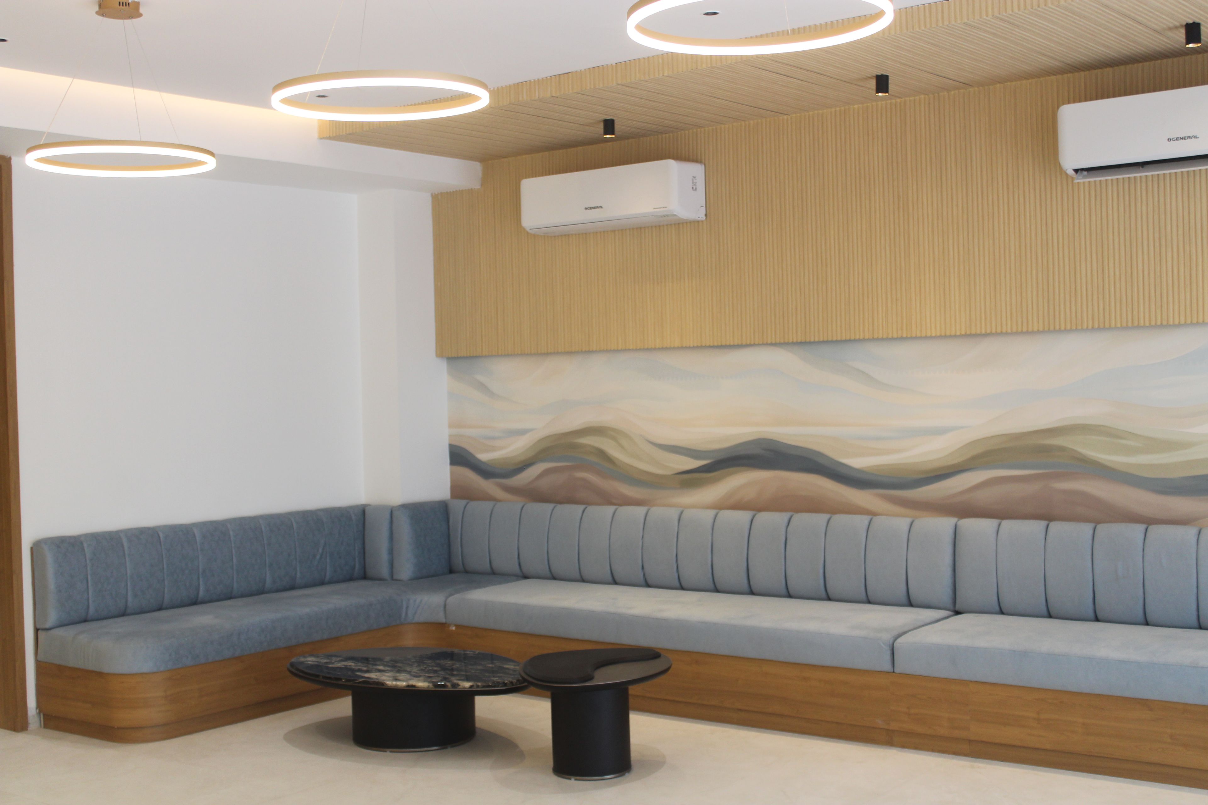 Un área de espera moderna con asientos en forma de curva, una mesita de centro y un aire acondicionado instalado en la pared.