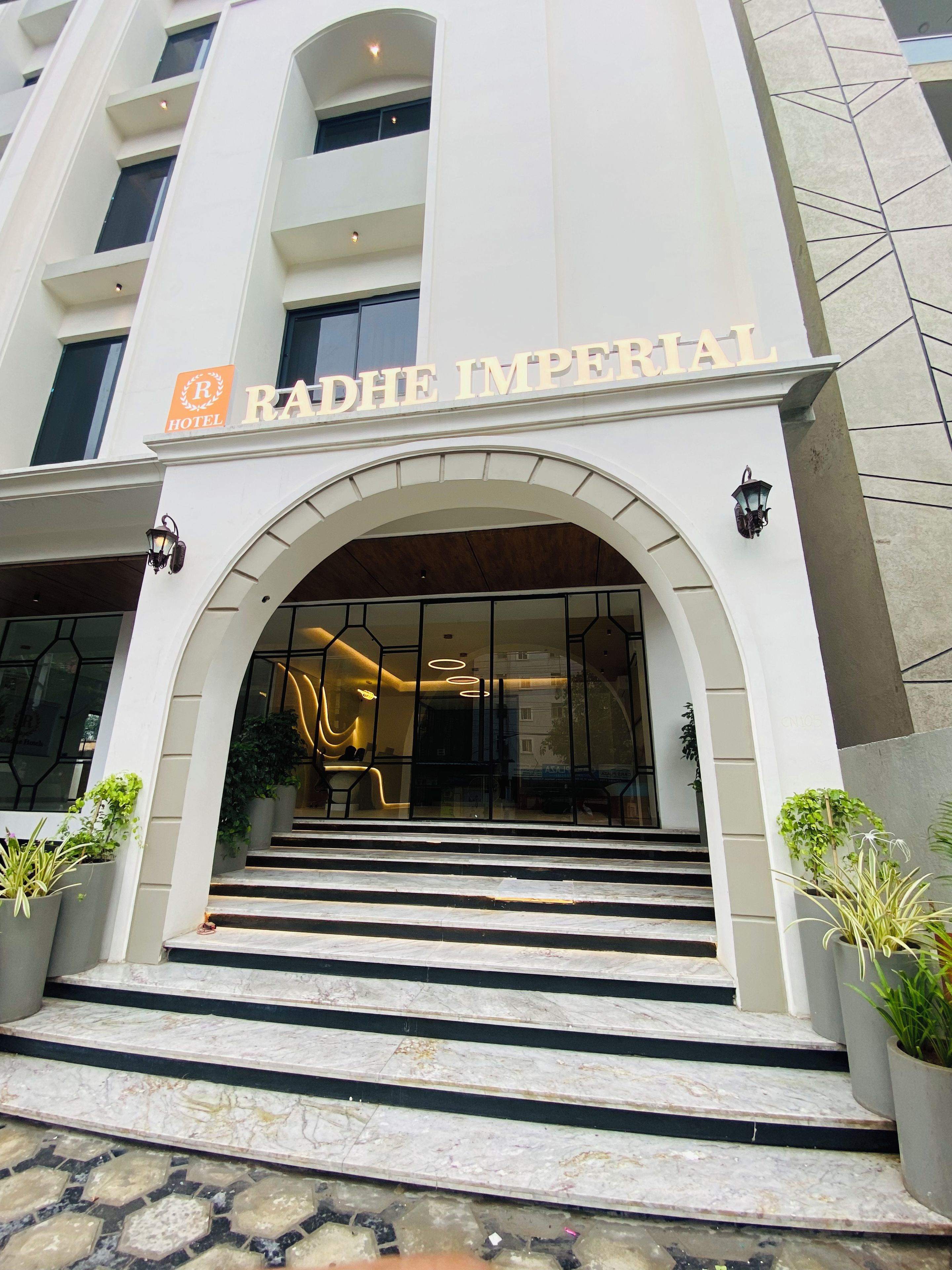 L'entrada de l'Hotel Radhe Imperial, de disseny modern, amb un gran arc d'entrada, escales de marbre i plantes en testos.