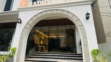 La entrada del Hotel Radhe Imperial con un diseño moderno, que presenta un gran arco, escalones de mármol y plantas en macetas.