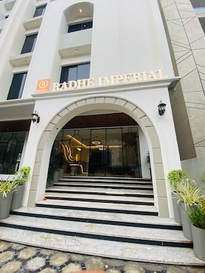 L'entrada de l'Hotel Radhe Imperial, de disseny modern, amb un gran arc d'entrada, escales de marbre i plantes en testos.