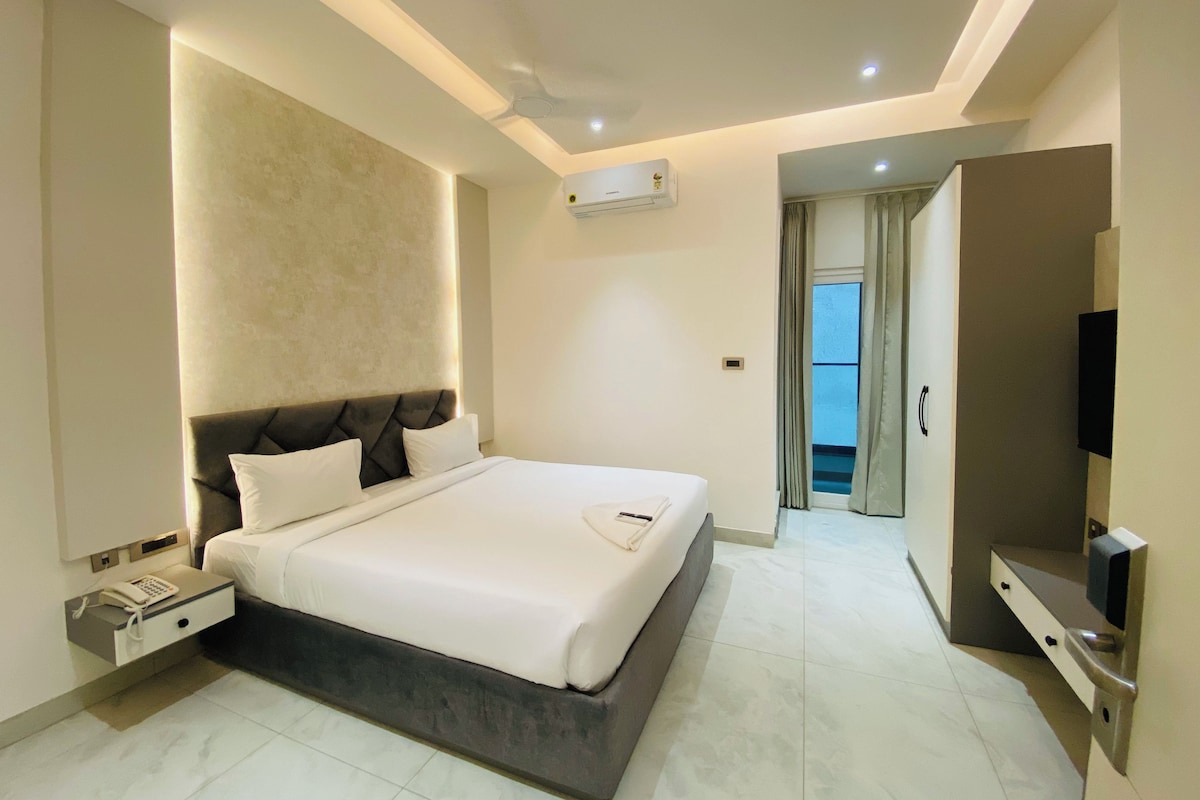 A modern hotel room with a large bed, a bedside telephone, a flat-screen TV, and a built-in air conditioning unit.