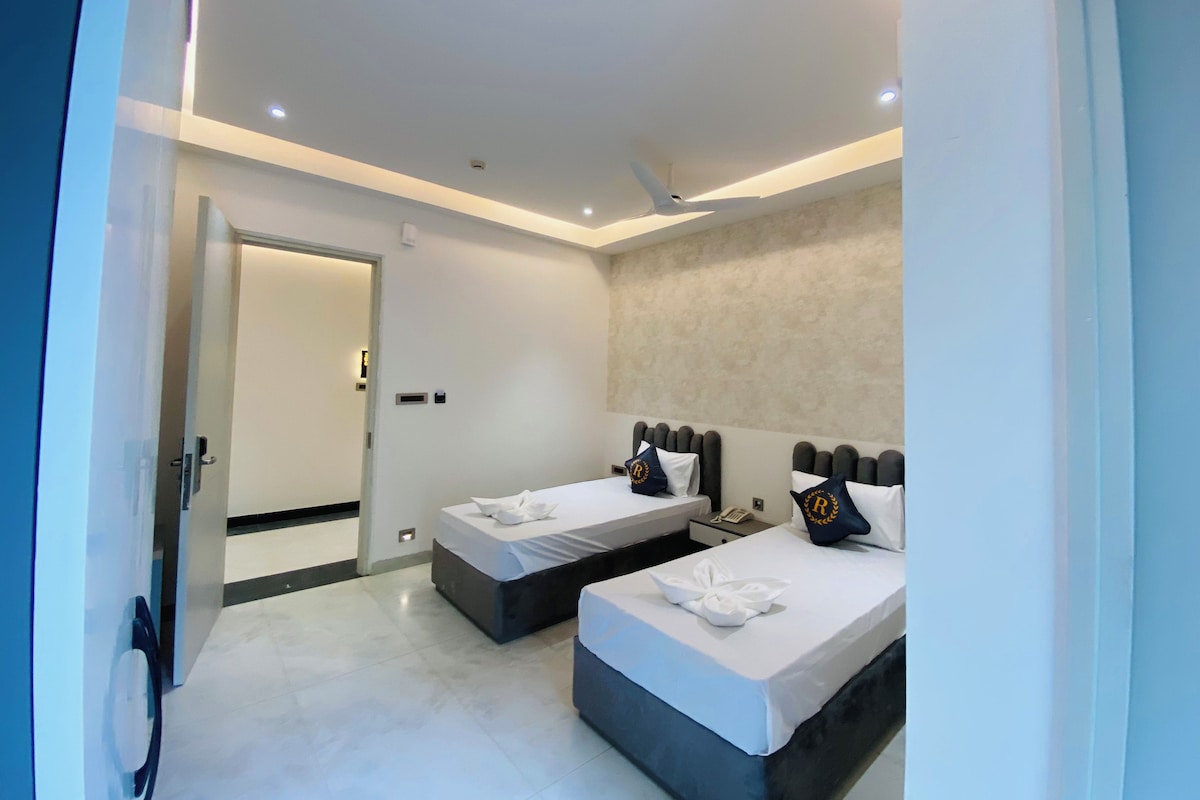 A modern hotel room with two beds, a bathroom, and a door leading to another room.