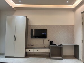 Una habitación moderna con una TV montada en la pared, un armario, un escritorio con silla y una cafetera.