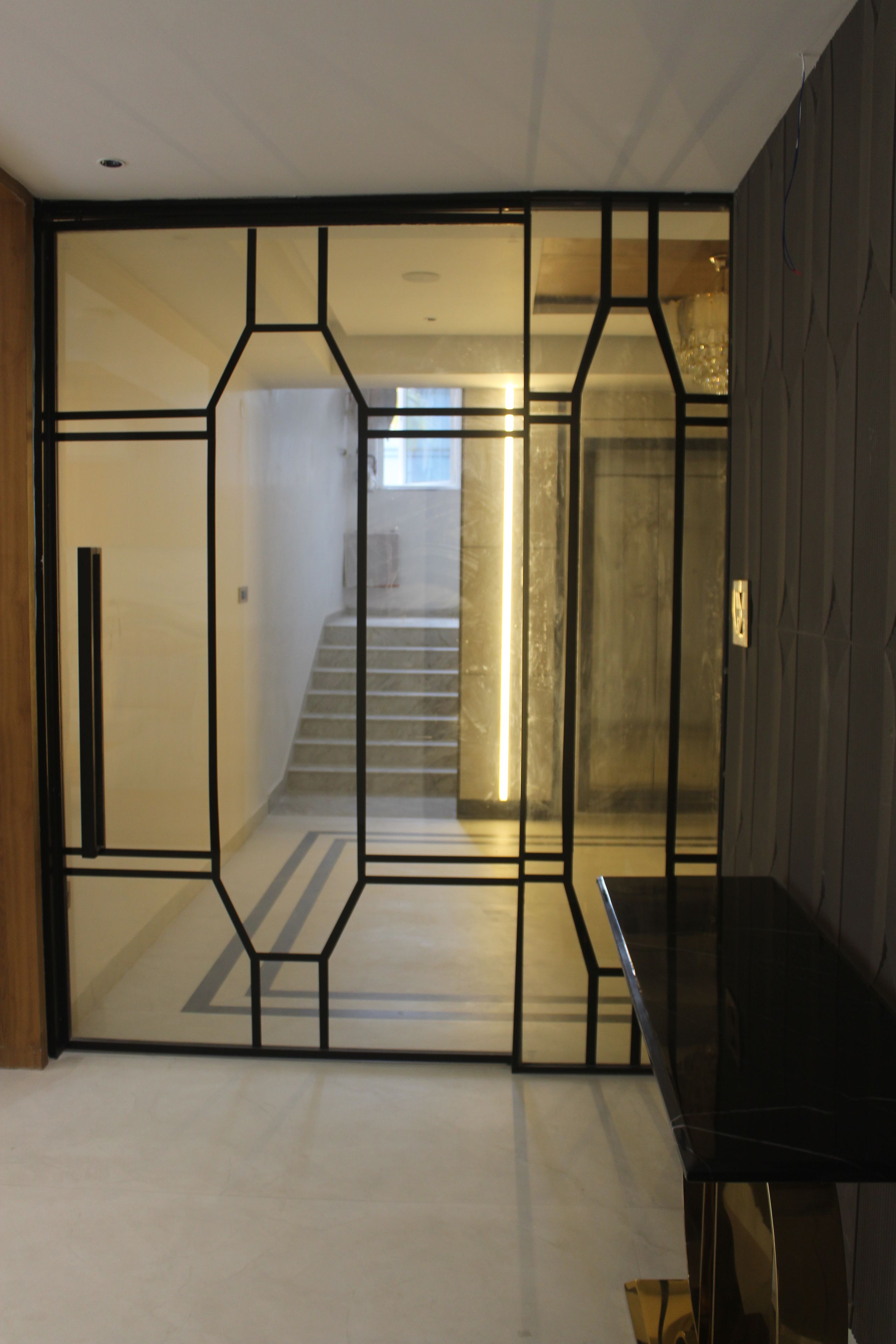 A room with a geometric-patterned partition, a staircase leading to an upper level, and a dark-colored furniture piece.