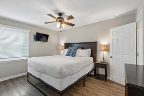 A bedroom with a bed, a ceiling fan, a television mounted on the wall, a bedside table with a lamp, and a door. - Atlantic High- 1 Summer Dunes-  Sleeps 22, PeekaBoo Views & Elevator! (Isle of Palms)