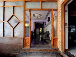 A hotel entrance with a wooden frame and glass panels, a marble floor, and a seating area with patterned cushions.