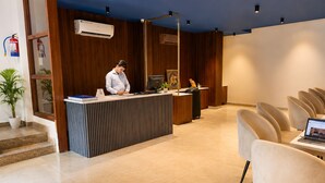 En reception med en receptionist, en computer og en skrivebordslampe. Der er stole og en potteplante i forgrunden.