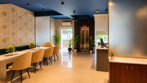 Et hotellobby med receptionsdisk, siddeområde med stole og et bord, samt en elevatorsektion.