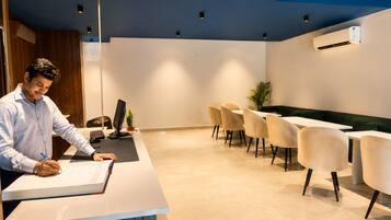 A reception desk with a person writing, a seating area with chairs and tables, and an air conditioning unit on the wall.