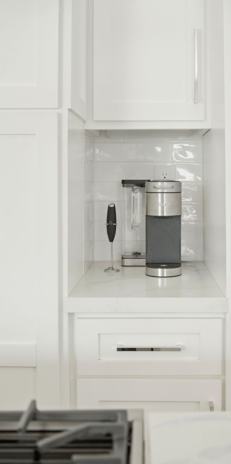 A kitchen with white cabinets, a wine glass, and a coffee maker on the countertop.