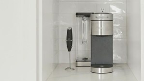 Keittiössä on valkoiset kaapit, viinilasi ja kahvinkeitin työtasolla.
