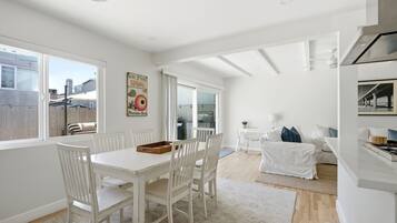 A spacious kitchen with white cabinetry, a dining area with a white table and chairs, and a living area with a sofa and a coffee table.