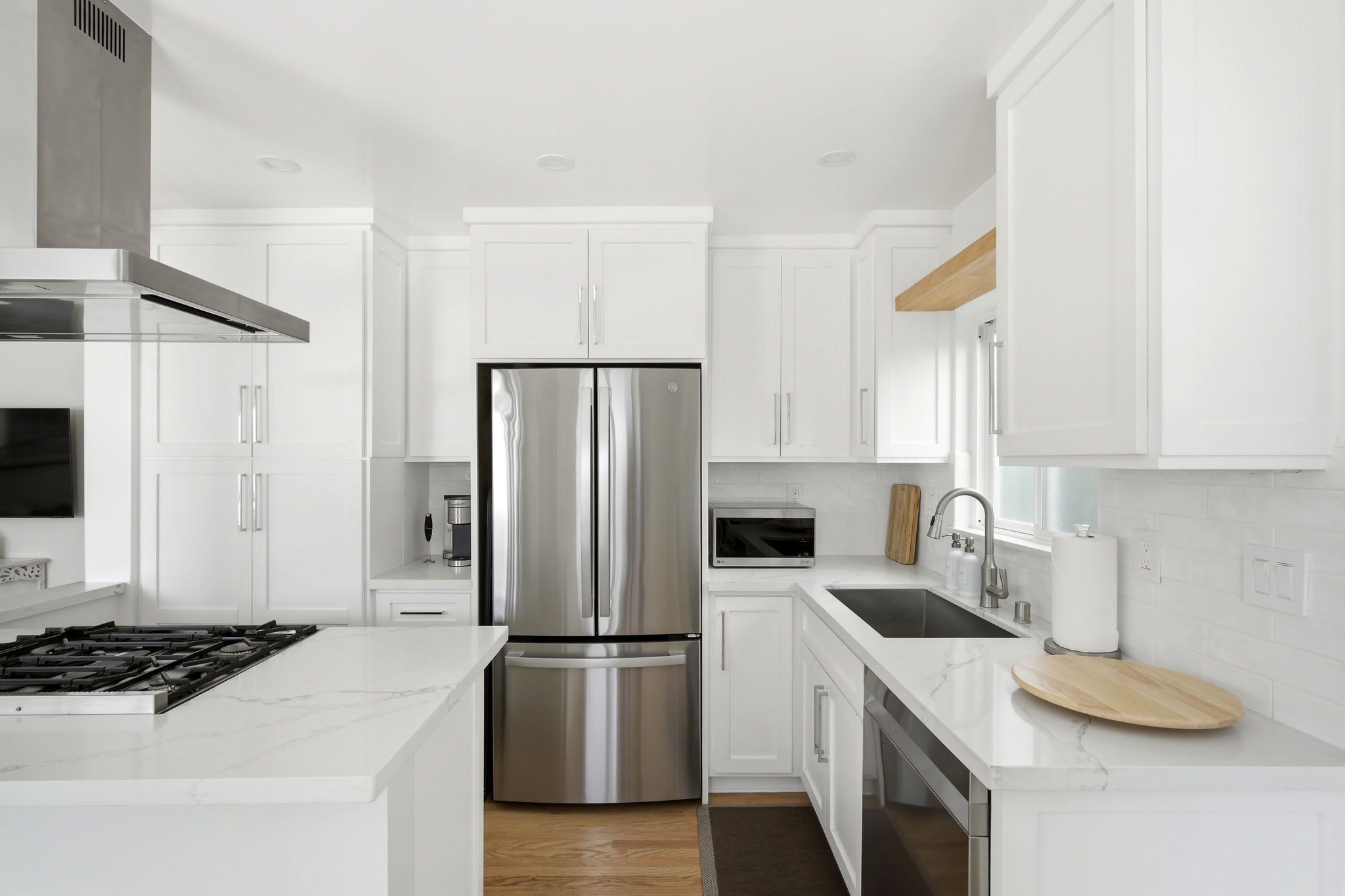 A modern kitchen with white cabinetry, stainless steel appliances, and a marble countertop.