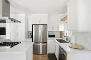 A modern kitchen with white cabinetry, stainless steel appliances, and a marble countertop. - Coastal Manhattan Beach Home | Walk to Beach & Downtown (Manhattan Beach)